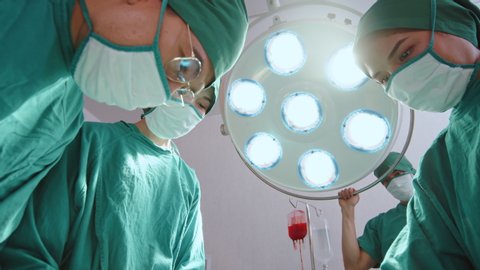 Group of Asian doctor, practitioner and nurse performing surgical operation in hospital's operating room, low angle view. Healthcare job, medical technology concept