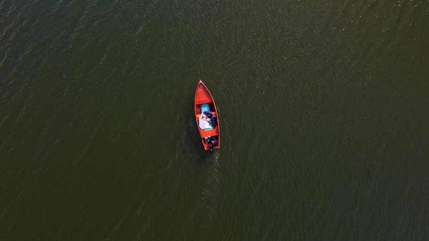 A wooden boat with newlyweds on board is sailing along the lake. View from top to bottom. Filming from the air with a drone. Water waves. Wedding in italy on lake como. Cinematic view with film noise