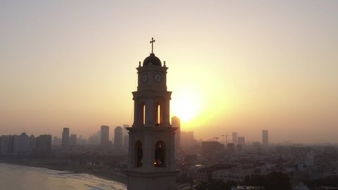 Sunrise flare striking Saint Peter church bell tower at Jaffa, Israel, Aerial view.