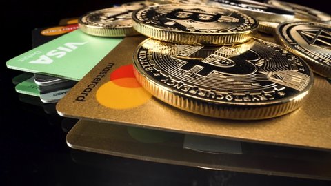 marbella , Málaga / Spain - 08 23 2020: Wide-angle macro view golden bitcoins coins and bank debit credit cards turning around on reflective black glass surface, cryptocurrency investment, MasterCard,