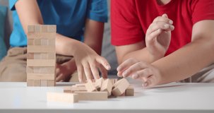 Close up of happy children sitting on grey couch and playing with wooden bricks. Little boy and girl in red and blue t-shirt making tower for entertainment at home.