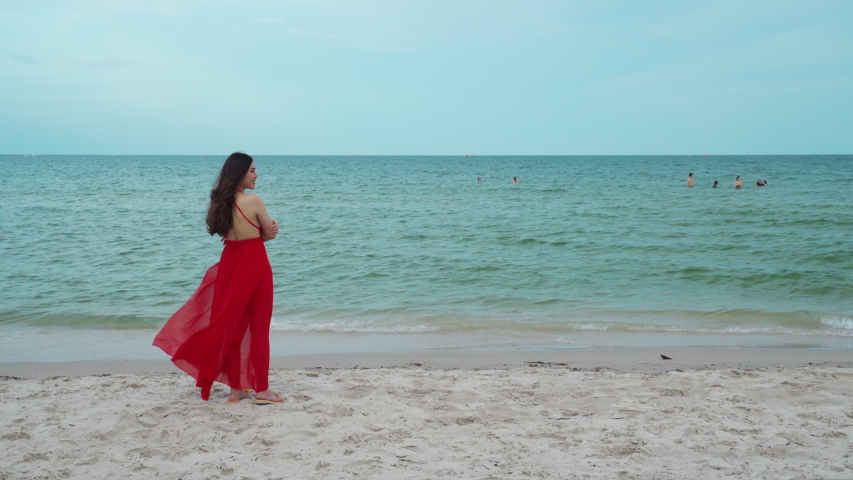happy woman in red dress standing with arms crossed on the sea beach with wind blow