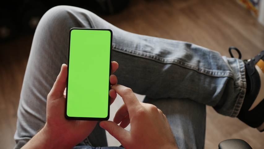 Man Using Smartphone in Vertical Mode with Green Mock-up Screen, Doing Swiping, Scrolling Gestures. Guy Mobile Phone, Internet Social Networks Browsing News, Financial Reports. Point of View Camera. Royalty-Free Stock Footage #1058296156