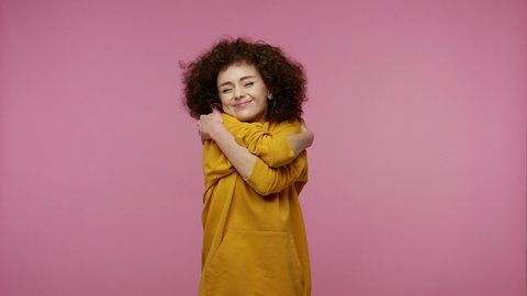 Come to me! Kind-hearted young woman afro hairstyle in hoodie outstretching hands with beckoning gesture, embracing herself to show how much she loves you and wants to hug. indoor  isolated, pink back