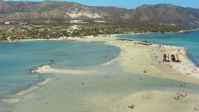Flies along Elafonisi Beach on Crete Island in Greece, tourists swim and relax, aerial video