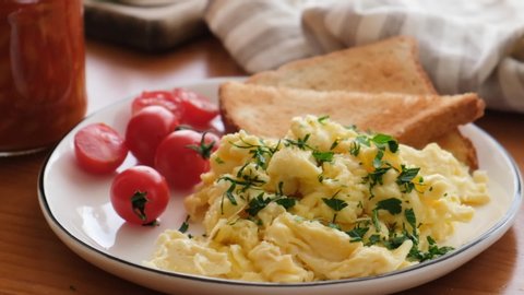Scrambled eggs garnished with chopped parsley. Eggs with toast and cherry tomatoes on plate. Breakfast food