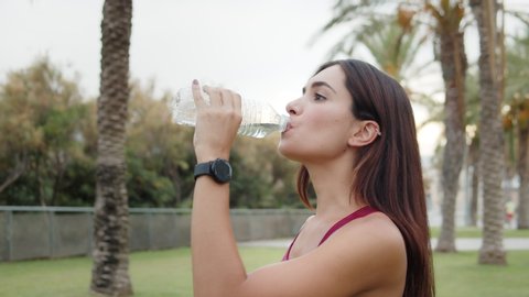 Hispanic woman drinking water from bottle after gym, outdoor workout, city sport, brunette latin girl drink clear mineral water after jogging. Generation z lifestyle.