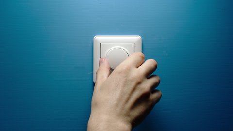 Human hand turns dimmer button on a blue wall slowly