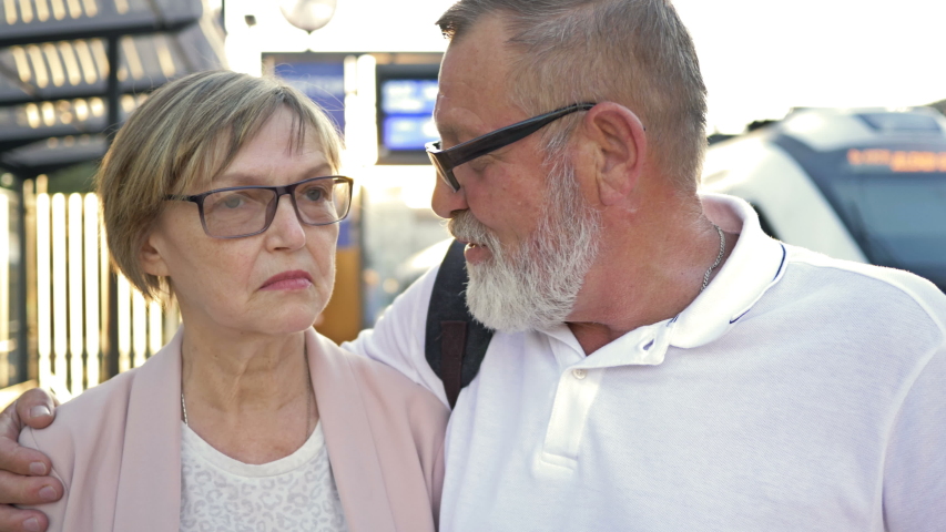 Cheerful elderly married couple standing on the platform waiting for their train.
