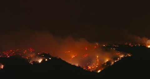Cinematic view on a fire at night. Heavy smoke causes air pollution and climate change disaster. Nature is on fire, red flames are visible in the dark, orange smoke is swirling above hot ground. 4K