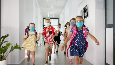 Group of cheerful children with face masks running on corridor, back to school concept.