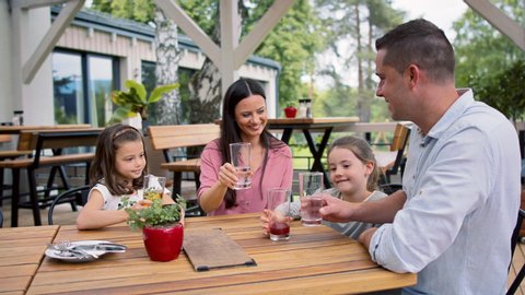 Family with children outdoors on terrace restaurant, clinking glasses.