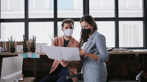 Portrait of young architects with face masks working indoors in office.