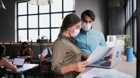 Portrait of young architects with face masks working indoors in office.