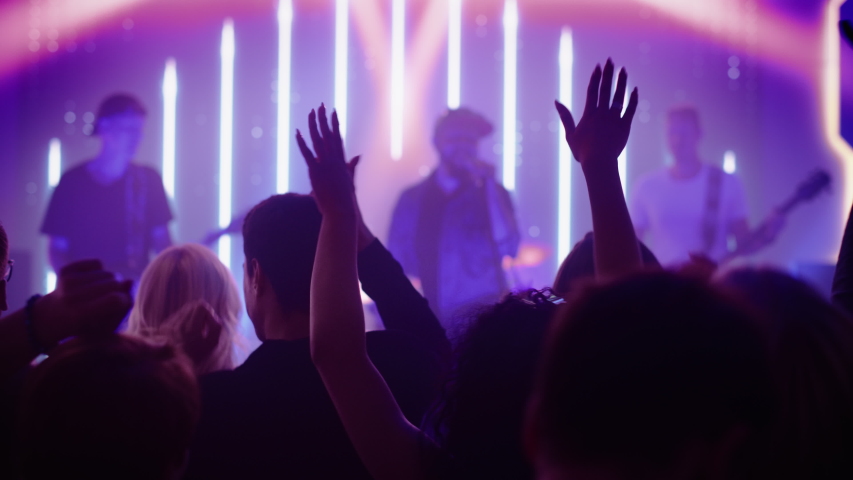 Rock Band with Guitarists and Drummer Performing at a Concert in a Night Club. Front Row Crowd is Partying. Silhouettes of Fans Raise Hands in Front of Bright Colorful Strobing Lights on Stage. - Powered by Shutterstock - Get 15% off with code: PIKWIZARD15