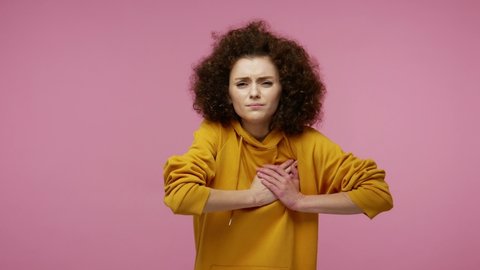 Cardiac problems. Young fatigued woman afro hairstyle in hoodie clasping chest, feeling acute pain, heart attack from anxiety, infarction symptom. indoor studio shot isolated on pink background