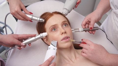 Close-up of a young woman's frightened look. Many hands hold cosmetic tools close to a woman's face.
