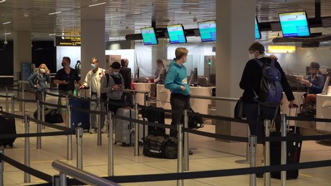 SCHIPHOL, NETHERLANDS – AUGUST 2020: Airline passengers wearing face masks stand in line at check-in desks at Amsterdam Schiphol Airport, international aviation during Covid-19 coronavirus pandemic