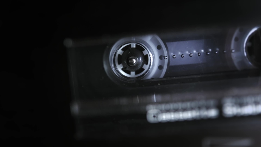 An audio cassette spools tape in extreme macro. Shallow depth of field with focus on the rorating spool. Suggests an interrogation or phonetap.  Royalty-Free Stock Footage #1058314954