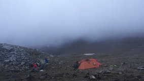 Tourist camp in the misty mountains in the evening. Evening turns into night. Tourists around the campfire and in tents. Time-lapse video.