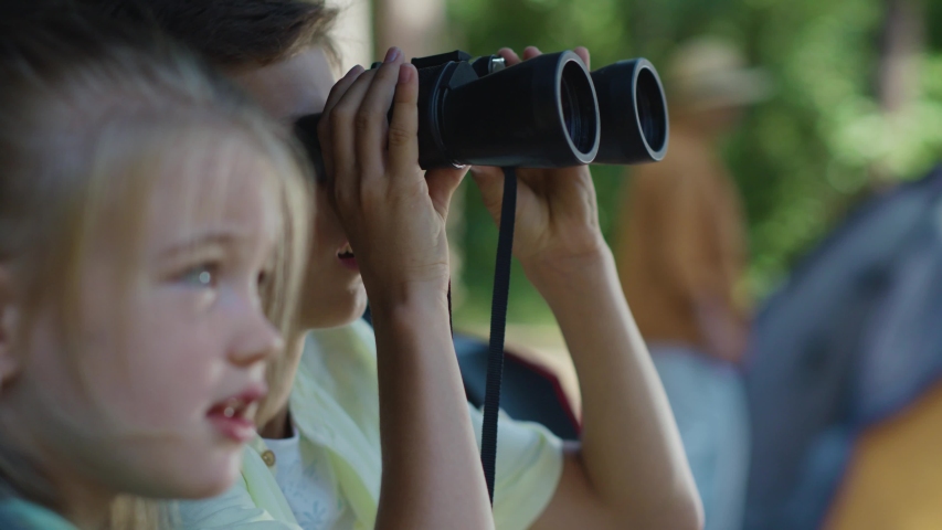 Two curious brother and sister using binoculars watching animals in the woods. Little explorers. Adventure. Camping in forest. Childhood concept.