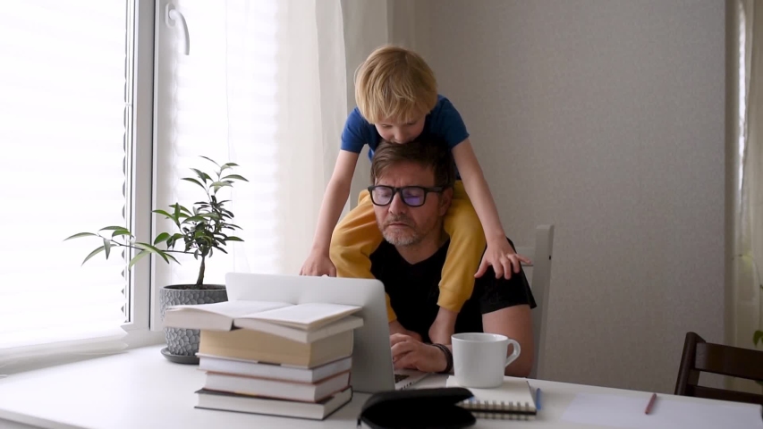 Man working from home with laptop during quarantine. Home office and parenthood at same time. Exhausted parent with hyperactive child. Chaos with kids during isolation Royalty-Free Stock Footage #1058326828