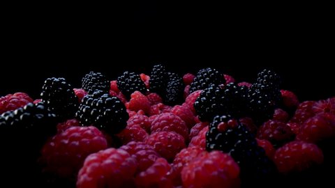 Blackberries and raspberries on a black background. Composition of a raw and fresh forest fruits close up in 4K.