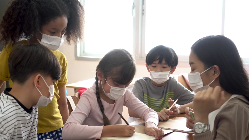 Group of diverse students in school building discussing in group study class. Elementary pupils are wearing a face mask while brainstorming. Covid-19 school reopen concept. | Shutterstock HD Video #1058326954