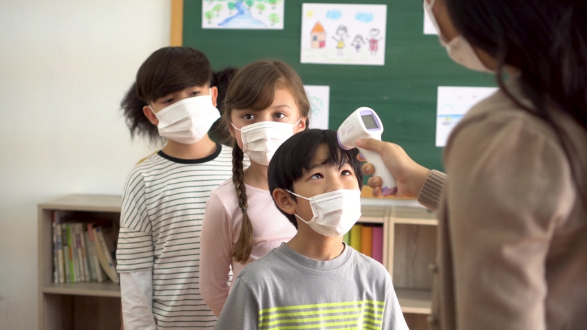 Group of diverse students in school building checked and scanned for temperature check. Elementary pupils are wearing a face mask and line up before entering into classroom. Covid-19 school reopen. Royalty-Free Stock Footage #1058326957