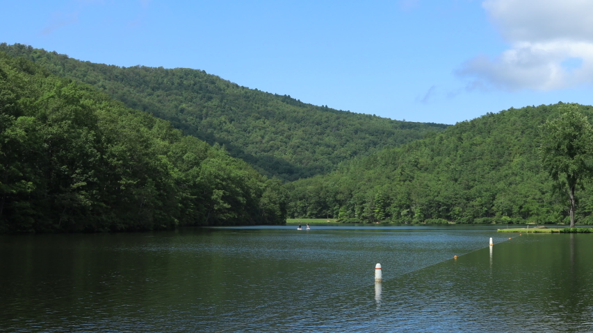 A blue sky summer day at Sherando Lake, part of the George Washington National Forest, in Virginia's Blue Ridge Mountains. Stand up paddleboard users and kayakers are seen paddling on the lake.