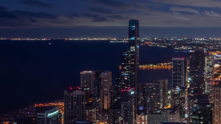 Zoom out night time aerial timelapse of Chicago skyline with pink and blue clouds in the sky floating over the water of Lake Michigan and the high rise skyscrapers in downtown along Michigan Avenue.