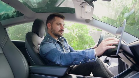 Good-looking modern 25-30-aged modern guy with well-groomed beard in jeans wears sitting in front of his auto's helm and applying navigator