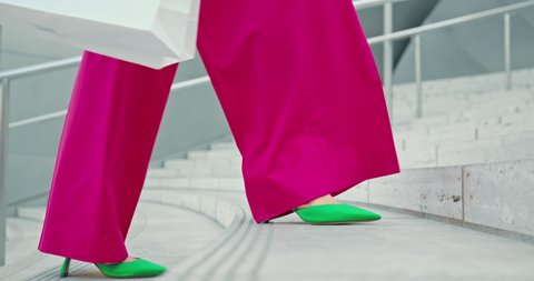 4K slow motion fashion. Close up woman in green fashionable heels walking up the stairs in downtown. Shopping concept footage, woman in hot pink trousers with white bags. Stylish girl legs on stairs