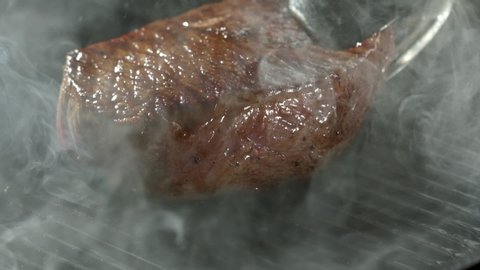 Piece of steak is fried on the grill pan. Close-up of chef flips juicy grilled meat steak, slow motion.