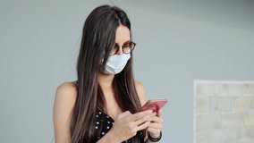 Video of beautiful young woman in face mask sending messages with her mobile phone while standing in the street.