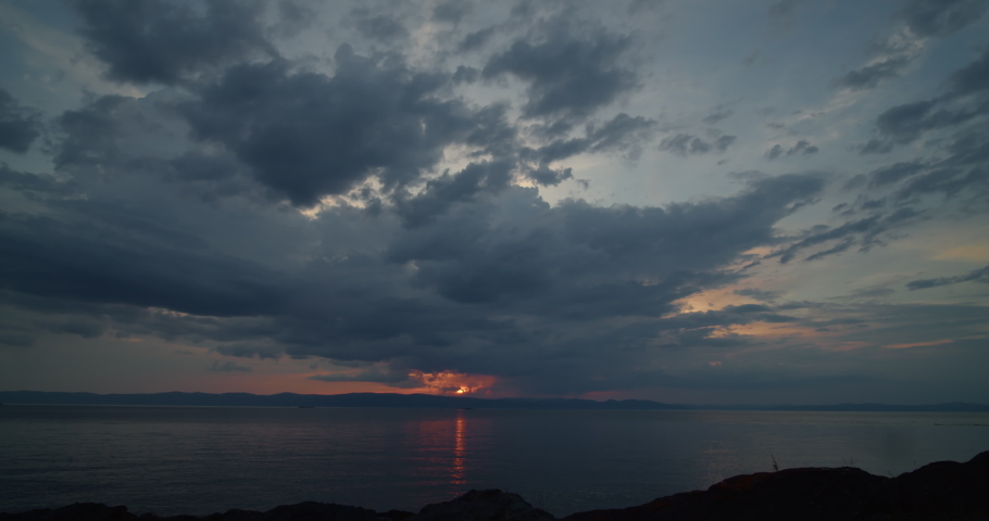 Dramatic clouds seen in the distance as sun sets below the horizon reflecting on a river in the foreground