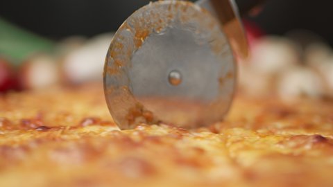 Cutting pizza with a round cutter knife. Close-up of delicious pizza being cut into pieces. Slow motion close-up of a person slicing a pizza into multiple slices with a cutter.