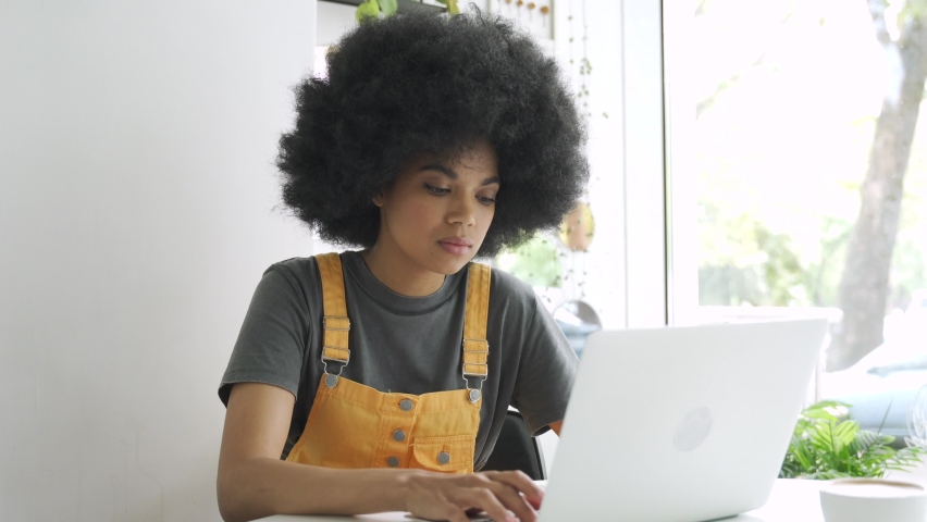 Young stylish hipster gen z African American female student with afro hair using laptop computer and smartphone sitting at table at home, in cafe, remote studying, elearning or working in internet. Royalty-Free Stock Footage #1058339587
