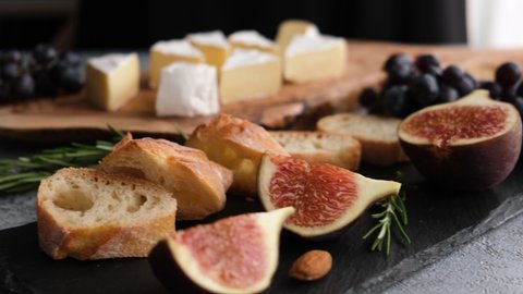 Cheese platter with camembert or brie cheese, figs, baguette and grapes. Woman's hand picking slice of camembert cheese. Wine appetizer set