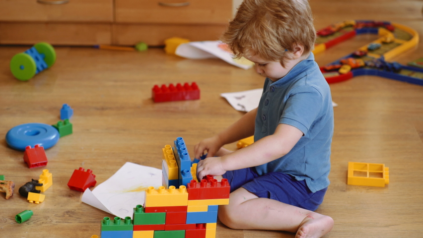 Funny curly baby boy with educational toy blocks. Children play at day care or preschool. Mess in kids room. Toddlers build a tower in kindergarten. Child playing with colorful toys. | Shutterstock HD Video #1058356429