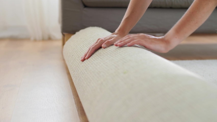 household, home improvement and interior concept - young woman unfolding carpet