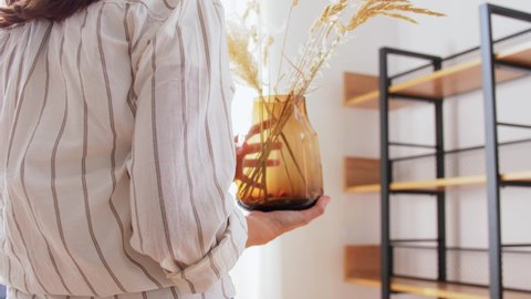 home improvement, decoration and people concept - woman placing dried flowers or herbs in vase to shelf