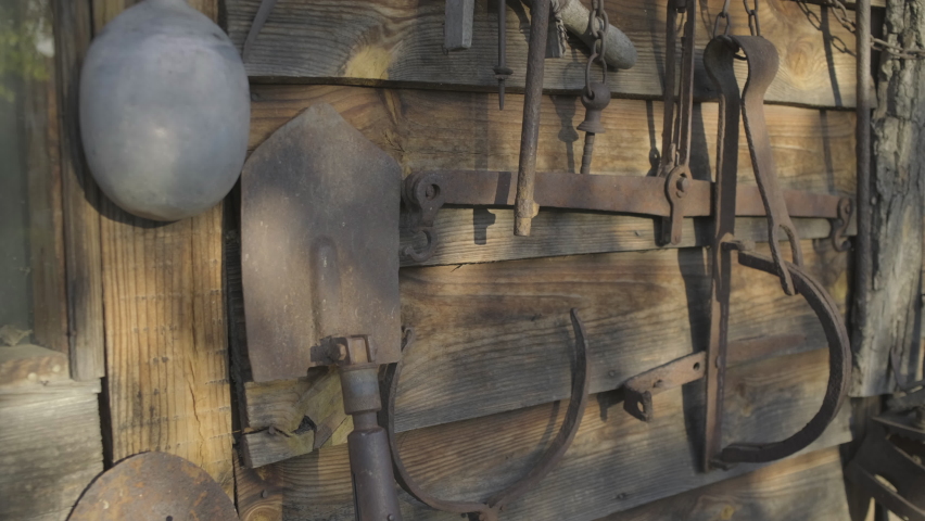 Obsolete rusty hunting equipment on the wooden wall. Old traps, shovel etc outside.