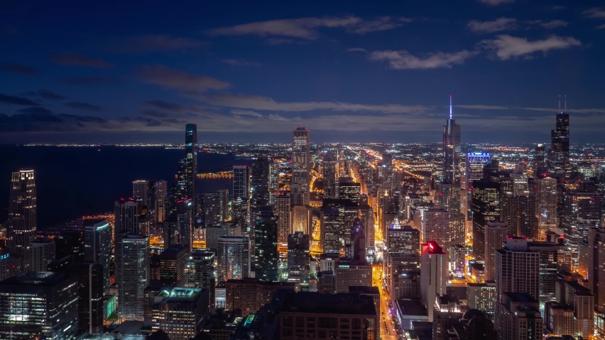 Beautiful night time aerial timelapse of Chicago skyline with pink and blue clouds in the sky floating over the water of Lake Michigan and the high rise skyscrapers in downtown along Michigan Avenue.