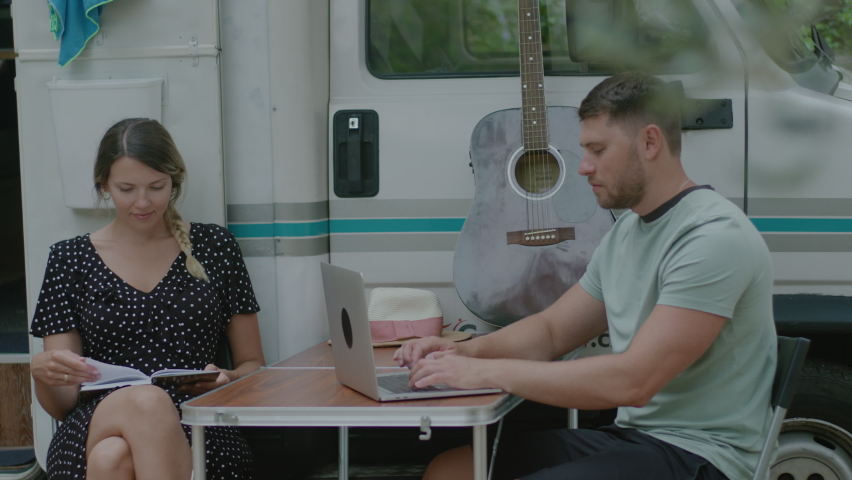 Traveler Man working at laptop and woman reading the book in summer camping. Tourist couple resting by mobile motor home RV campervan  in Montenegro.
