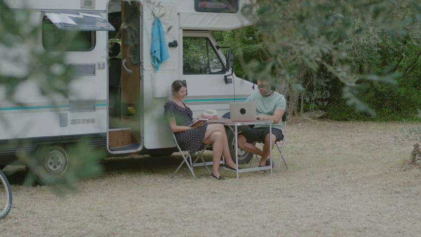 Traveler Man working at laptop and woman reading the book in summer camping. Tourist couple resting by mobile motor home RV campervan  in Montenegro.
 | Shutterstock HD Video #1058364943