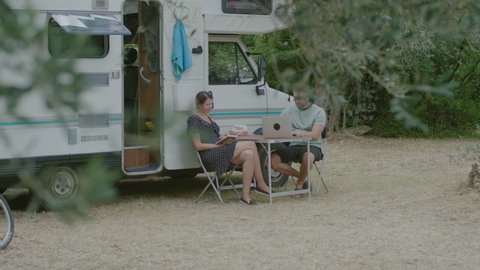 Traveler Man working at laptop and woman reading the book in summer camping. Tourist couple resting by mobile motor home RV campervan  in Montenegro.
