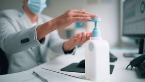 Handsome Stylish Young Man Wearing Protective Face Mask Uses Hand Sanitizer while Working at His Desk on a Computer in Office. Young Male Follows Health and Safety Instructions. Slow Motion - Powered by Shutterstock - Get 15% off with code: PIKWIZARD15