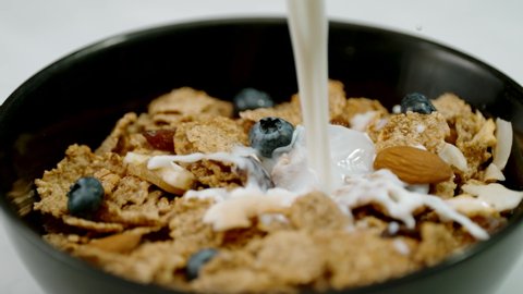 Slow motion milk pour on a healthy cereal bowl filled with fruit and nuts 