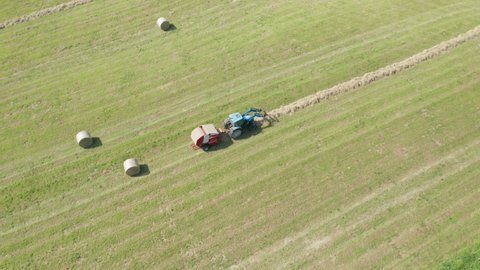 Aerial view of blue tractor with round baler discharging a fresh hay bale during harvesting